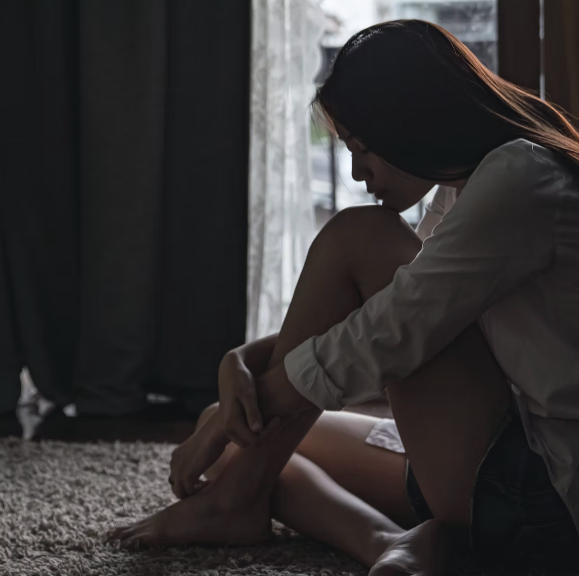 Foto: Frau sitzt zurückgezogen am Fenster – Symbolbild zu Emotionen und Nervensystem